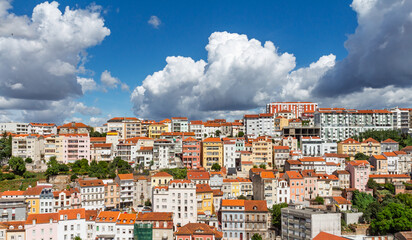 Colorful residential houses stacked on the hillside in Coimbra, Portugal, featuring diverse architecture under a dramatic blue sky with clouds.