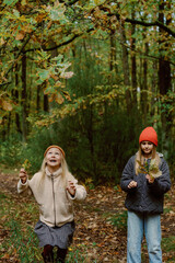 Fototapeta premium Two children enjoy a wonderful afternoon in a colorful autumn forest, surrounded by golden leaves. They laugh and collect leaves, embracing the beauty of nature.