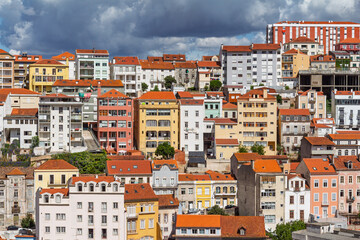 Detailed view of dense, colorful apartment buildings and houses on the steep slopes of Coimbra, Portugal, showing urban architectural diversity.