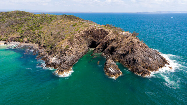 Aerial view of the rugged, rocky cliffs of Hell's Gates meet the turquoise waters, a stark contrast to the lush greenery above, Noosa Heads, Queensland, Australia.