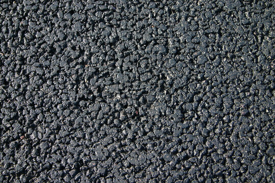 Black asphalt road texture. A top-down view of fresh dark bitumen pavement with a coarse granular aggregate surface.