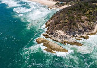 Aerial view of the rugged coastline where emerald waters crash against the rocky cliffs of Point Lookout, Queensland, Australia.