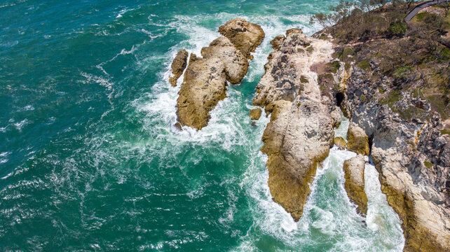 Aerial view of waves crashing against the rugged cliffs of Point Lookout, the turquoise water contrasting with the golden rocks, Point Lookout, Queensland, Australia. - Powered by Adobe