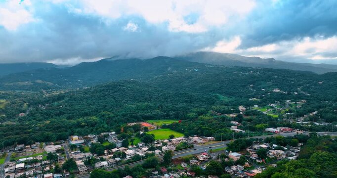 Cityscape of Puerto Rico surrounded by the verdant hills with lush greenery. Grey clouds float over the city. Aerial view.