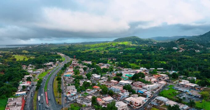Lively roads cross the cityscape of modern Puerto Rico. Drone footage over the beautiful scenery with lots of lush greenery. Thick clouds cover the sky.