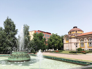 Beautiful architectural landmark in the center of Sofia, the capital of Bulgaria. Front yard with sprinkling fountain in front of palace. Sightseeing in European cities. Cultural heritage admiration.