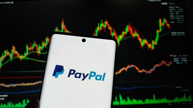 Closeup of paypal logo on smartphone screen against a backdrop of a stock market trading chart, representing digital finance and investment trends  , New York City, 15 December 2025