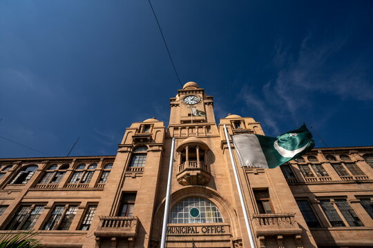 View of the Municipal Office building with its clock tower under a clear sky, the flag of Pakistan waving in the wind, Karachi, Sindh, Pakistan.