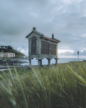 View of a weathered Galician h&oacute;rreo stands sentinel against the moody sky, its stone facade a stark contrast to the vibrant green grass, Baiona, Pontevedra, Spain.