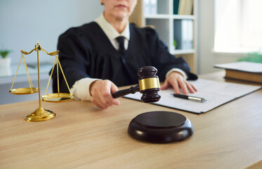 Female judge, wearing robe, holding gavel in legal office, scales of justice at desk, document,...