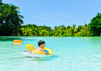 One 7 years old Asian boy swimming in pool with a life buoy in tropical resort