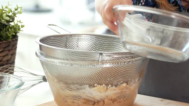Little girl baker sifts flour through a sieve