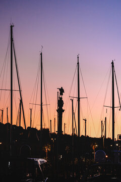View of the silhouetted masts of yachts punctuate the vibrant twilight sky above the Christopher Columbus monument, Barcelona, Catalonia, Spain.