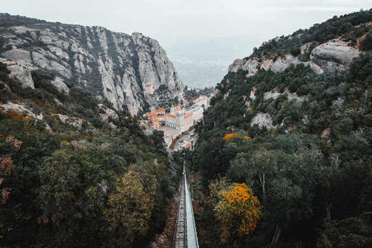 View of the ancient monastery nestled between jagged cliffs and verdant forests, with a funicular cutting through the landscape, Montserrat, Catalonia, Spain.