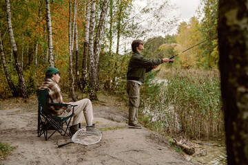 Two friends spend a calm afternoon fishing by the river. One casts a line from the shore while the...