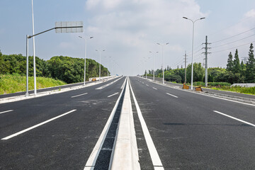 Fototapeta premium Empty newly paved asphalt road stretching into the distance under a clear sky.