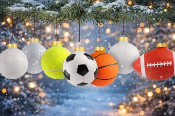 Sports-themed Christmas ornaments shaped like different balls hanging fully visible from snow-covered fir branches, with warm bokeh lights and a festive winter background.