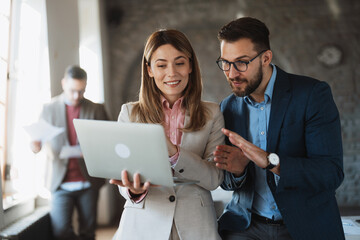 Young female professional explaining digital data on a computer screen to a coworker with another colleague in the background.