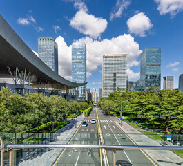 Fototapeta premium Modern city street with skyscrapers and green trees under a blue sky in Shenzhen.