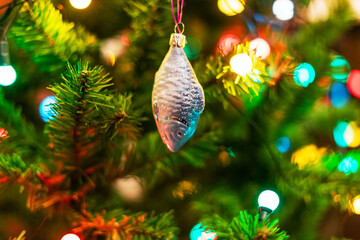 Christmas tree decorated with glass toy fish ornament and colorful garland lights, New Year celebration
