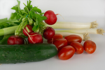 Assorted fresh vegetables from home garden including radishes, cucumbers, cherry tomatoes, and green onions, isolated on white background for healthy food concepts.