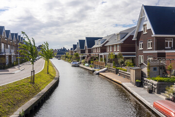 View of tranquil canal reflecting the modern brick houses under a soft sky, boats gently bobbing near wooden docks, Leiden, South Holland, Netherlands.