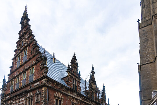 View of old majestic brick building with intricate detailing and a towering spire against a backdrop of cloudy skies, Haarlem, North Holland, Netherlands.