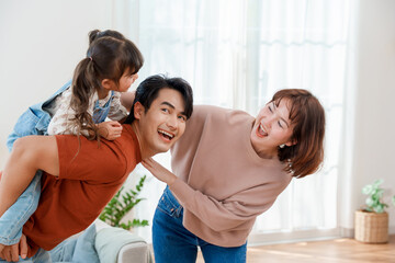 Happy Asian family having fun at home with father giving a piggyback ride to his little daughter...