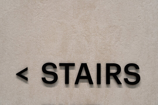 Minimalist interior wall with black STAIRS lettering and arrow sign on beige textured concrete surface, modern architectural wayfinding detail