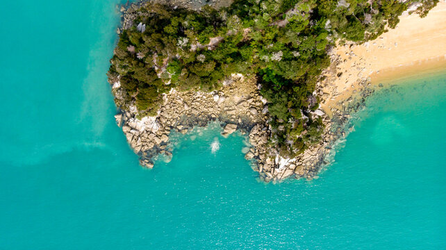 Aerial view of a rocky outcrop meets the turquoise sea in Abel Tasman National Park, Tasman Region, New Zealand.