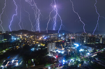 View of electrifying lightning bolts illuminating the night sky over the cityscape with bright city lights below, Mumbai, Maharashtra, India.