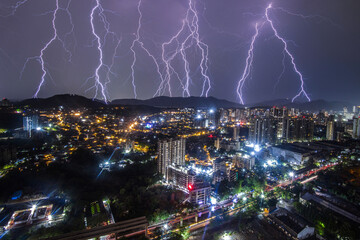 View of electric lightning bolts dramatically illuminate the night sky over the city's skyline and distant mountains, Mumbai, Maharashtra, India.