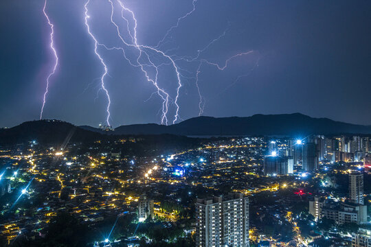 View of electric lightning bolts illuminate the night sky above the cityscape with vibrant strikes, casting an eerie glow over the buildings, Mumbai, Maharashtra, India.