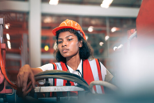 Professional Black African female factory engineer/worker/technician operate machinery in modern industrial plant. She wear safety helmet,vest show focus,skill in repair maintenance production process