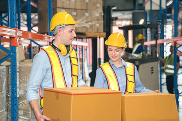 White Man and woman warehouse worker wear safety helmets, safety vests carry cardboard box in industrial factory storage inventory. Show teamwork efficient modern logistics, supply chain management