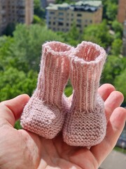 Hand holding two pink knitted baby booties. The boots are knitted and have a pink color