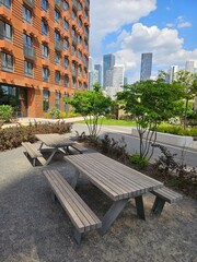 Wooden picnic table with two benches and a city skyline in the background. The table is located in a park near entrance in the courtyard of the house in residential complex