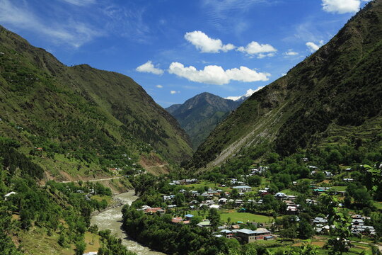 View of the valley with a river snaking through the base surrounded by lush green mountains, a small village nestled amidst the landscape, Neelum Valley, Azad Kashmir, Pakistan.