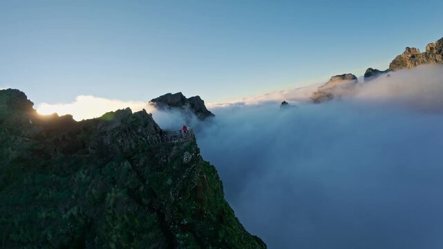 Flying over the clouds at Pico do Arieiro at sunset on the island of Madeira, Portugal. Magical sunset view above the clouds flying near mountain ranges and hikers.
