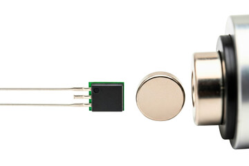 Electronic magnetic sensor chip next to round metal magnet on a transparent background