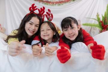 Three children celebrate Christmas holiday with joyful expressions on bed