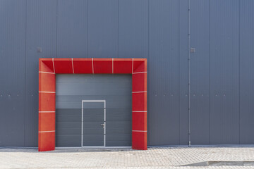 Modern industrial warehouse facade with gray metal wall, sectional roller door and integrated pedestrian door, framed by a bright red geometric arch, minimal architecture background.
