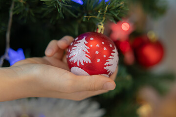 Woman hand holds a bright red Christmas ornament decorated