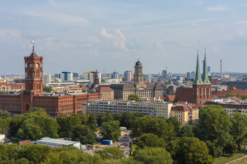 View of Rotes Rathaus buildings and Nikolaikirche spires rise above lush green trees under a bright sky, painting a vibrant cityscape, Mitte, Berlin, Germany.