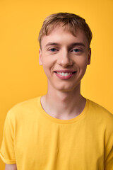 Young smiling male in a yellow t shirt against a bright studio background, conveying casual style,...