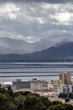 View of buildings nestled beneath a brooding sky, where mountains fade into the horizon and the sea reflects the somber light, Cagliari, Sardinia, Italy.