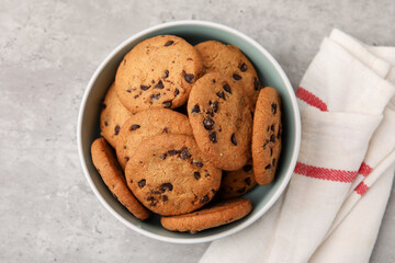Delicious chocolate chip cookies in bowl on gray textured table, top view
