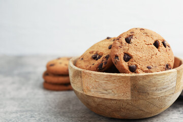 Delicious chocolate chip cookies in bowl on gray textured table, closeup. Space for text