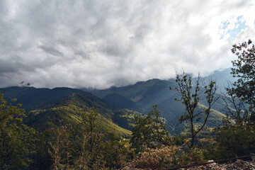 Mountain landscape with forested hills under a cloudy sky, expansive natural scenery featuring rugged terrain, lush trees, and a tranquil atmospheric view