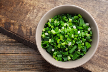 Bowl with cut green onions on wooden table, top view